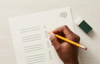 O que é System One, a categoria de IA do Jev Mão feminina de pele negra clara segura lápis amarelo sobre prova minimalista com desenho de cérebro e borracha branca com capa verde escuro